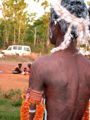 A man in a traditional dress is standing in a dirt field, symbolizing the importance of male rites of passage and the coming of age.