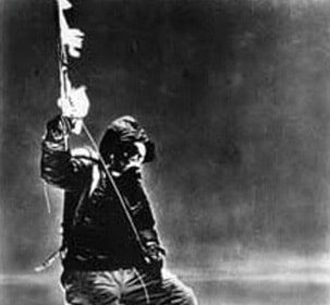 An adventurous man triumphantly stands atop a majestic mountain, proudly holding a flag.