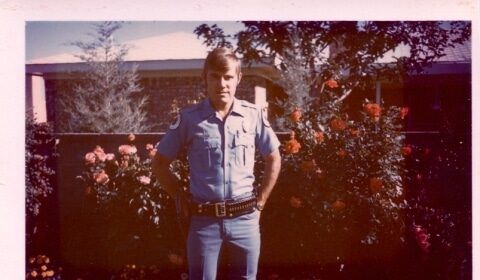 A Game Warden in a police uniform standing in front of flowers.