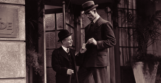 Two well-dressed men in suits and hats are standing next to each other.