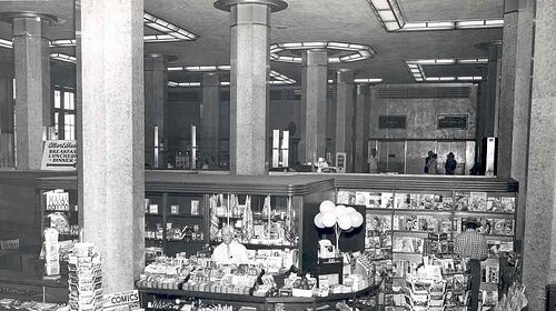 A black and white photo of a store with shelves displaying magazines.