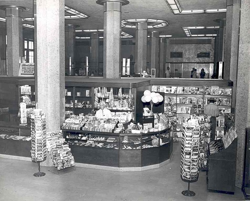 A black and white photo of a store with shelves displaying magazines.