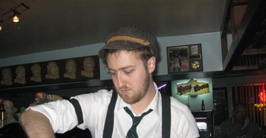 A bartender in suspenders pouring a bottle of wine.