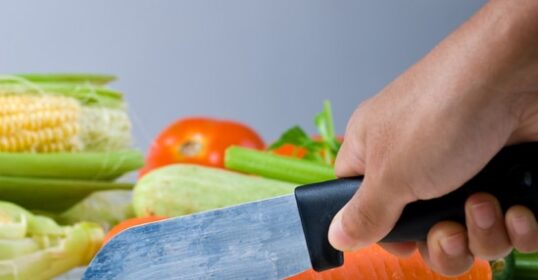 A person using a knife to cut vegetables on a cutting board.