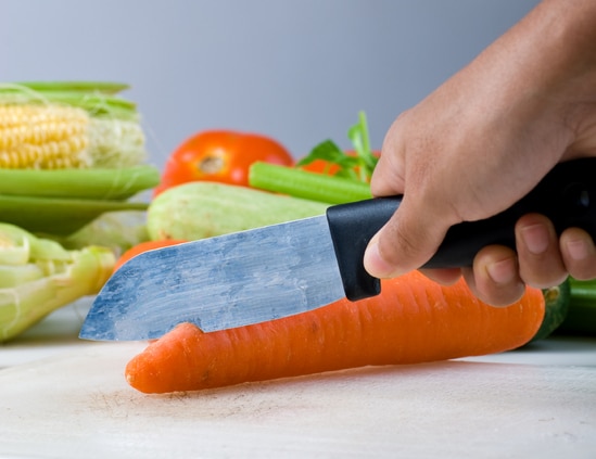 A person using a knife to cut vegetables on a cutting board.