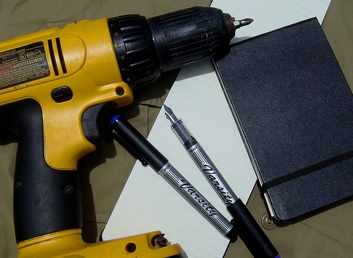 Cordless electric drill with fountain pens and notebook.