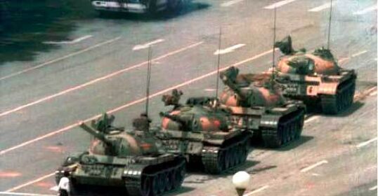A group of developing tanks on a street in front of a man exhibiting manly courage.