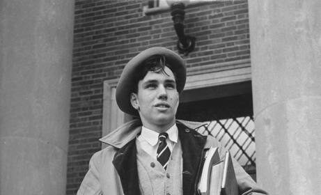 A man in a coat and hat standing on the steps of a building exuding manliness.