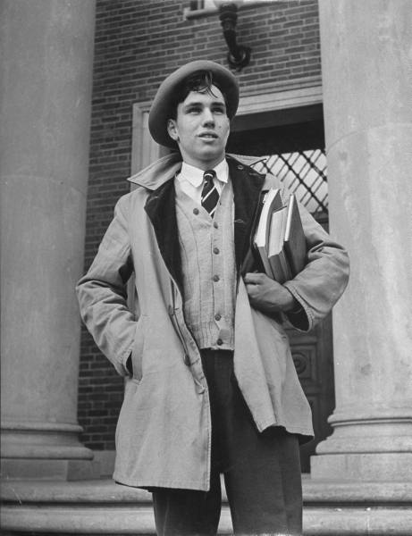 A man in a coat and hat standing on the steps of a building exuding manliness.