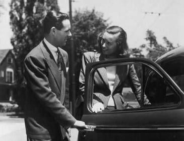 A man and woman writing next to a car door.