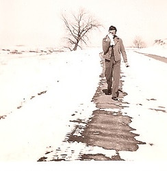 A man walking down a snow-covered road in an old photo.