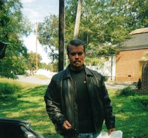 A private investigator in a leather jacket standing next to a car.