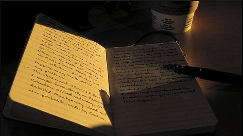 A moleskine notebook on a table with a cup of coffee next to it.