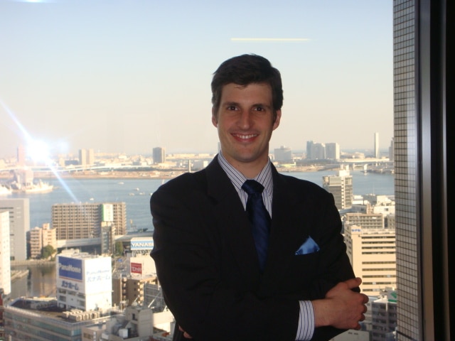 A man in a suit standing in front of a city view, appearing as an interpreter or translator.
