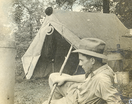 Vintage man lying outside the tent and holding stick.