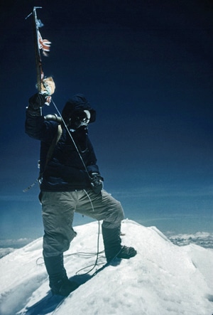 Man standing on the peak of a snow mountain holding a flag.