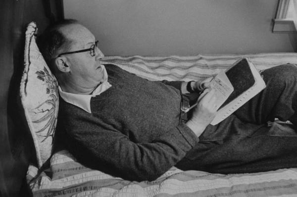 A vintage man laying on the bed and writing on the paper.