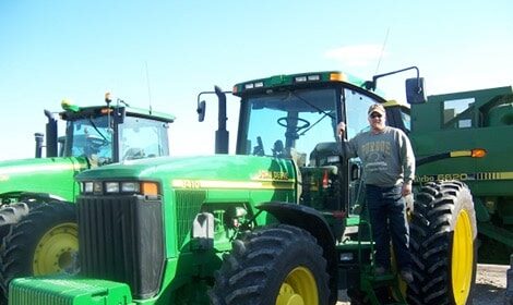 A farmer standing next to a green John Deere tractor.