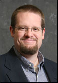 A college professor with glasses and a beard smiling.
