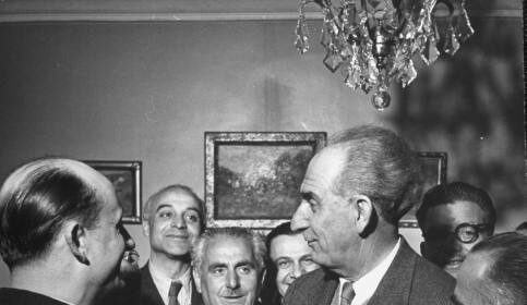 A man in a suit and tie is commanding a room full of men.