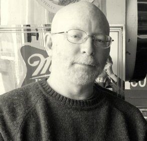 A bald man with glasses in a black and white photo.