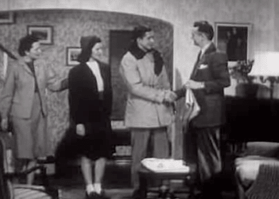 An old black and white photo of a group of parents in a living room.