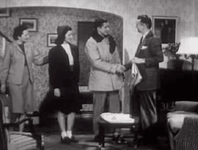 An old black and white photo of a group of parents in a living room.