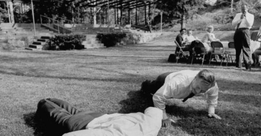 Two men performing ultimate push-up exercises in the grass.