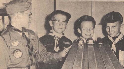 A group of scouts building their 1st place Pinewood Derby Car next to a wooden board.