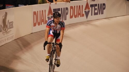 A cyclist racing on a bicycle track in front of a crowd.
