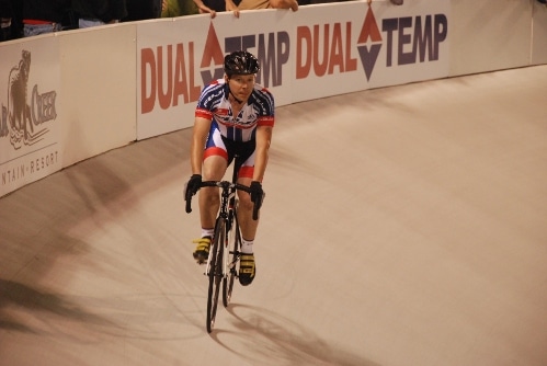 A cyclist racing on a bicycle track in front of a crowd.