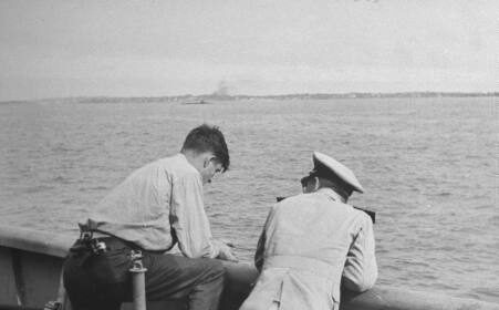 Two men, one of them a man, standing on the deck of a ship.