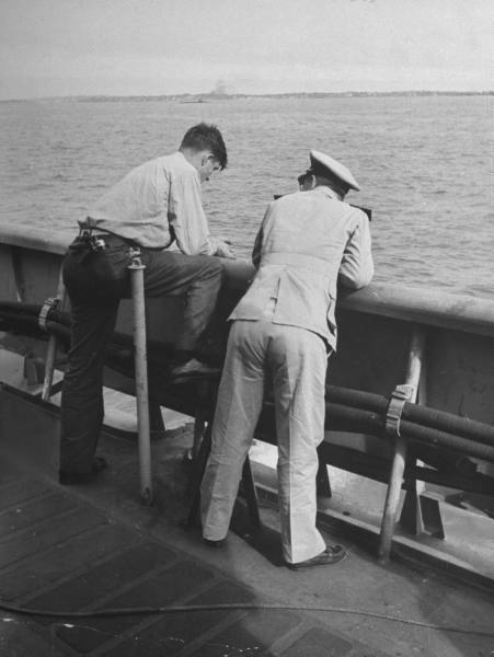 Two men, one of them a man, standing on the deck of a ship.