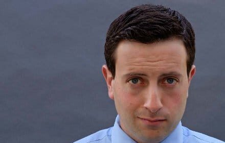 An actor in a blue shirt and tie making a fist gesture in his job.