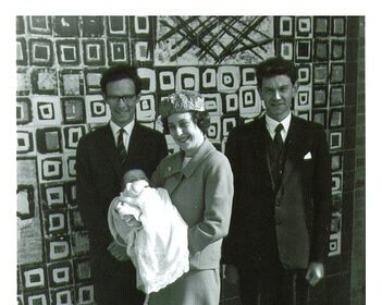 Three great individuals standing in front of a tiled wall with a baby in their arms.