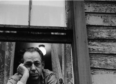 A black and white photograph capturing the raw emotion of a man leaning out of a window, expressing his grief and loss.