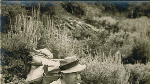A man engaged in international backpacking, sitting on a hillside with his backpack.