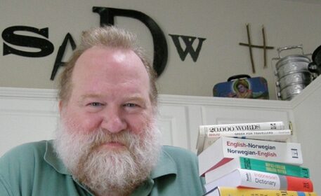 A bearded Name Consultant standing next to a stack of books.