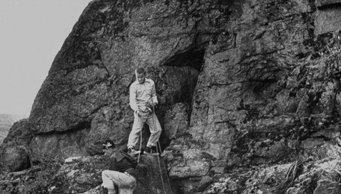 Two men conquering difficulties while climbing up a rocky cliff, displaying manvotional determination.