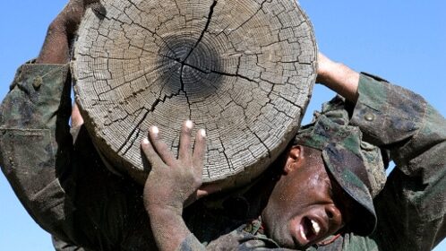 A Navy Seal is carrying a large piece of wood, embodying the creed.