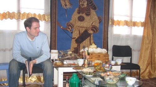 A Peace Corps Volunteer sitting in front of a table with food on it.