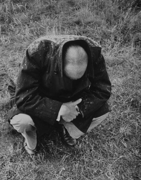 Black and white photograph of a man dealing with male depression while kneeling in the grass.