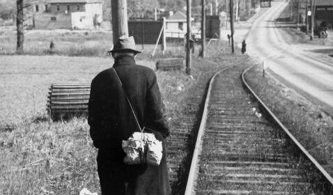 A hobo walking down the railroad tracks in an old black and white photo.