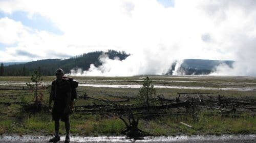 A man backpacking near a geyser.