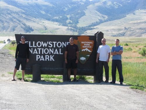 Jeff Rose posing along with his friends in front of Yellowstone national park entrance board.