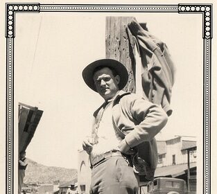 A man in a cowboy hat exuding manliness as he leans against a pole.
