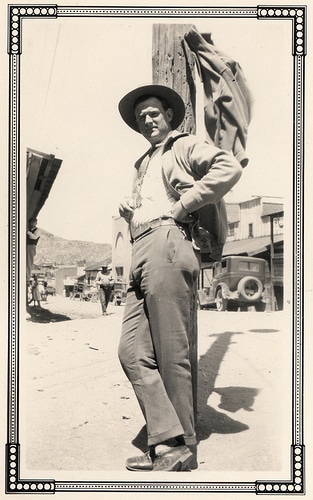 A man in a cowboy hat exuding manliness as he leans against a pole.