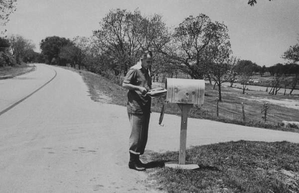 Vintage man getting mail from mailbox beside the road.