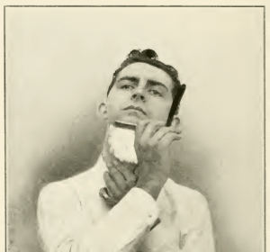 An old photo depicting a man expertly shaving his beard with a straight razor.