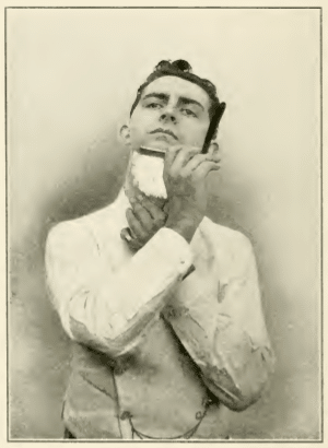 An old photo depicting a man expertly shaving his beard with a straight razor.
